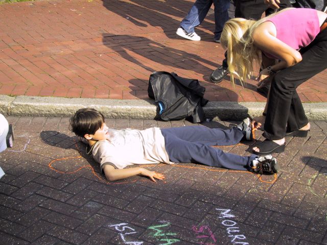 A boy lies down whilst his outline is chalked around